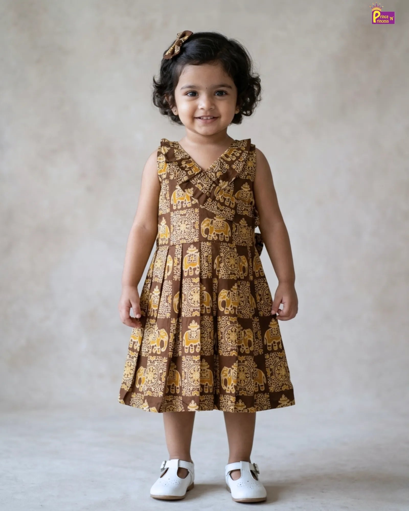 Young girl wearing a brown dress with gold patterns against a plain background
