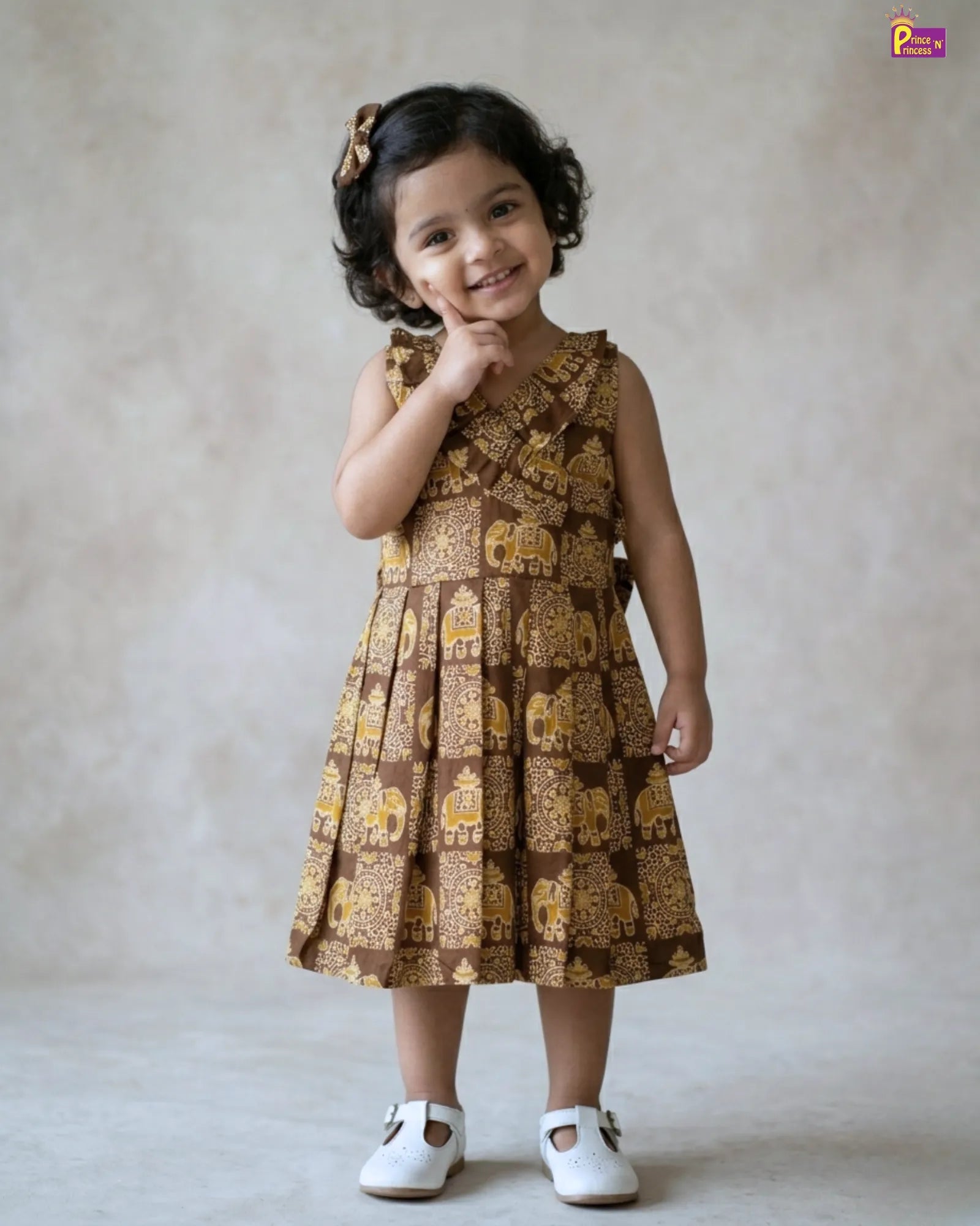 Young girl wearing a brown and gold patterned dress against a plain background