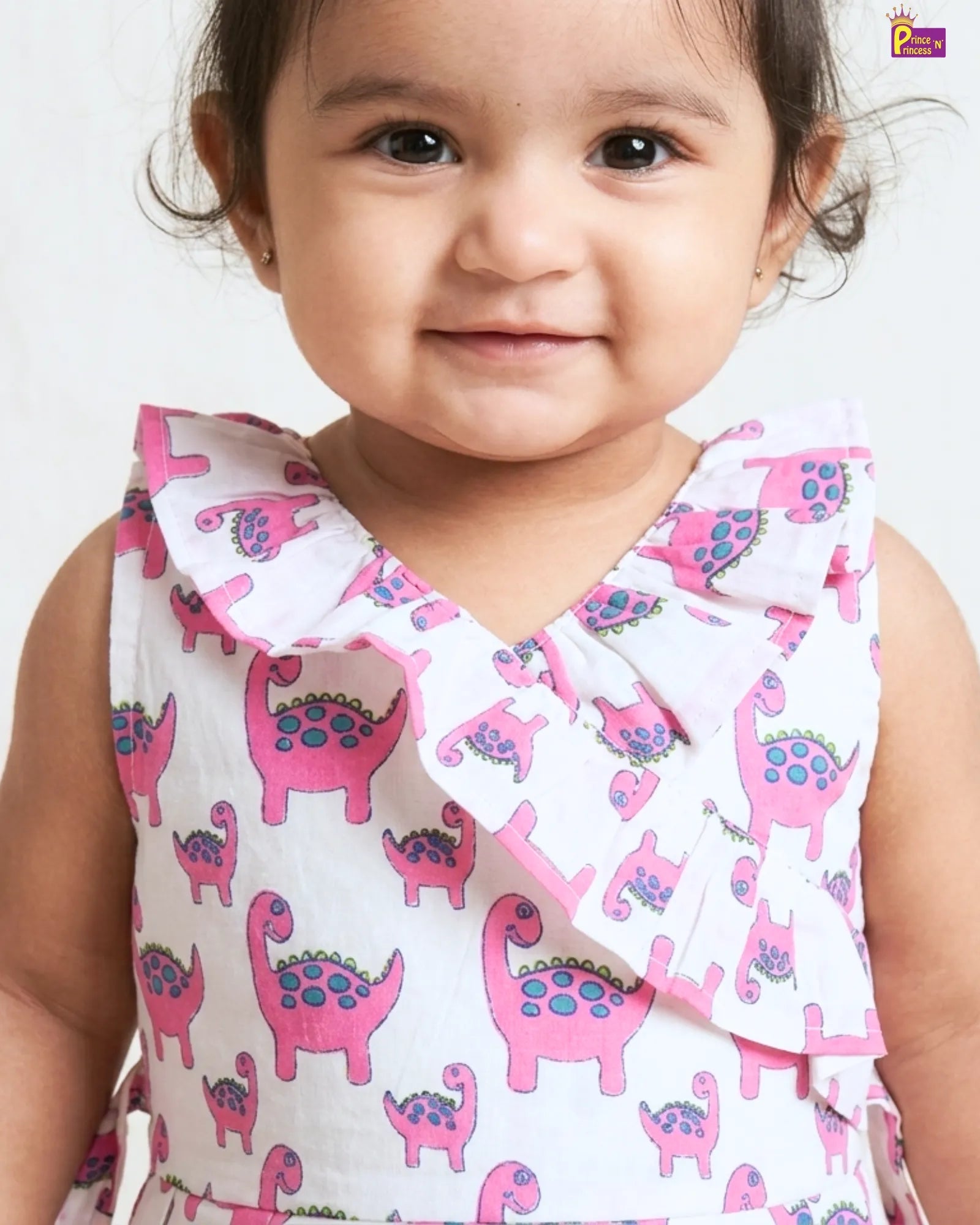 Child wearing a dress with pink dinosaur pattern on a white background