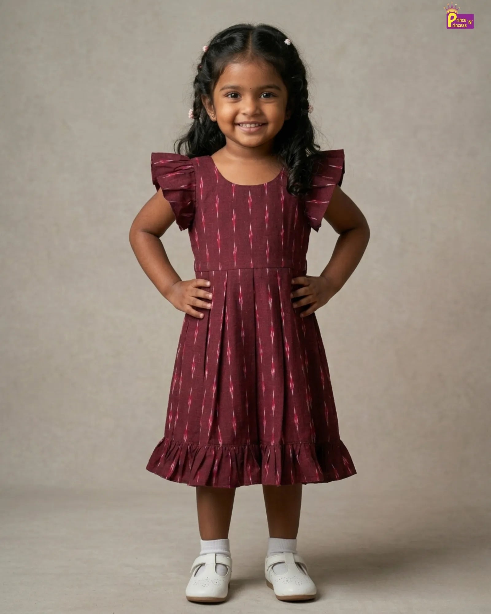 Young girl wearing a maroon dress with ruffled sleeves against a neutral background