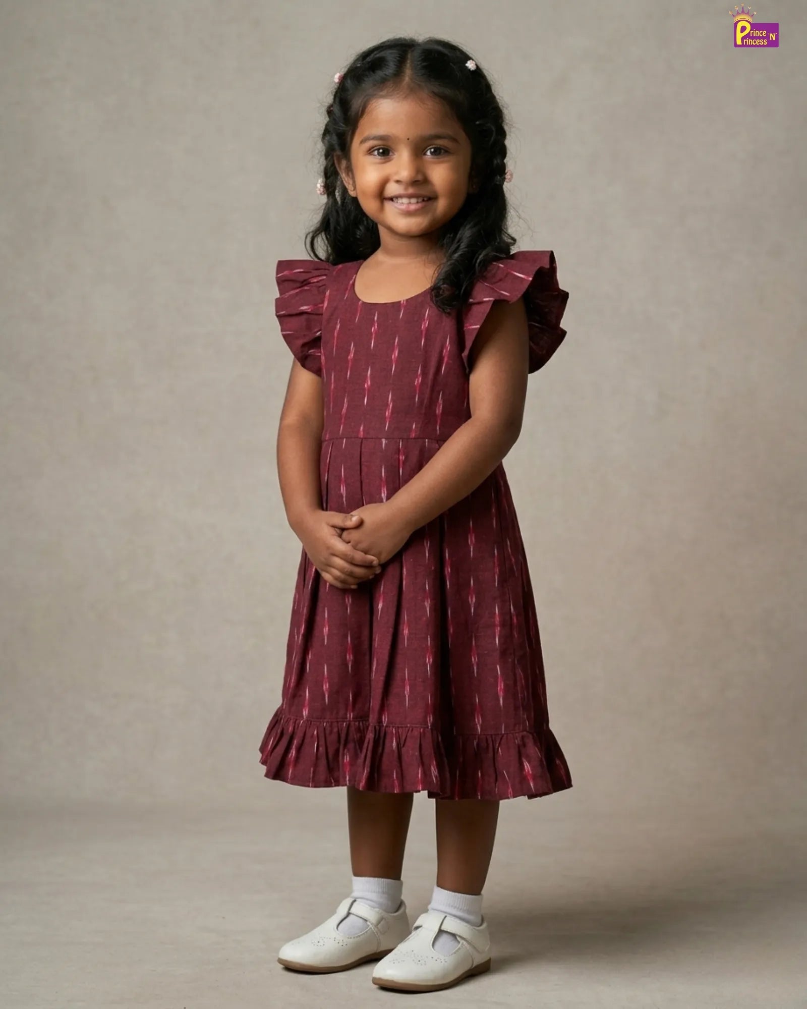 Young girl wearing a maroon dress with ruffled sleeves against a neutral background