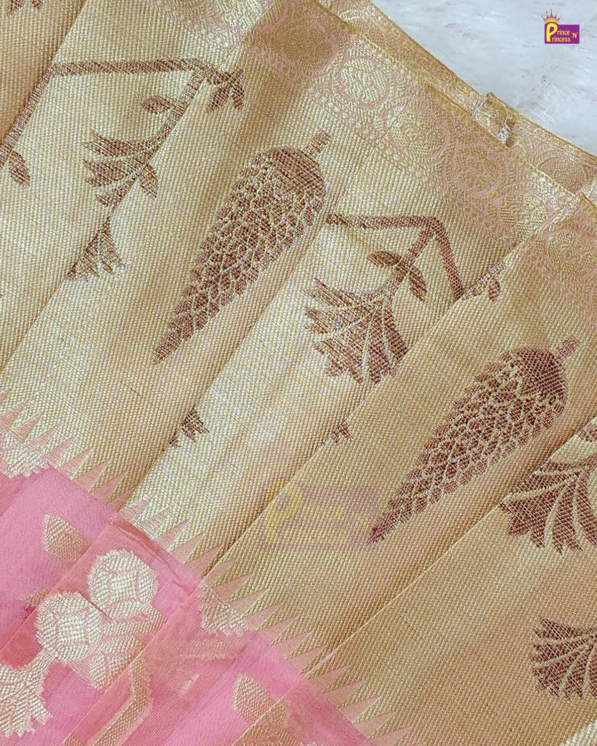 A close-up of a beige and gold saree fabric with woven botanical motifs, featuring a pink border with gold floral details.