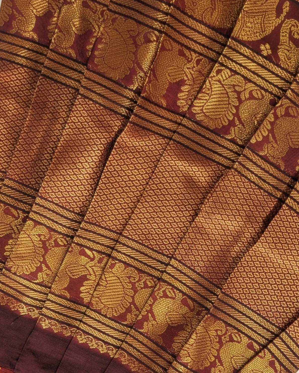 Close-up of a richly patterned fabric with metallic gold woven motifs and borders over a deep maroon background.