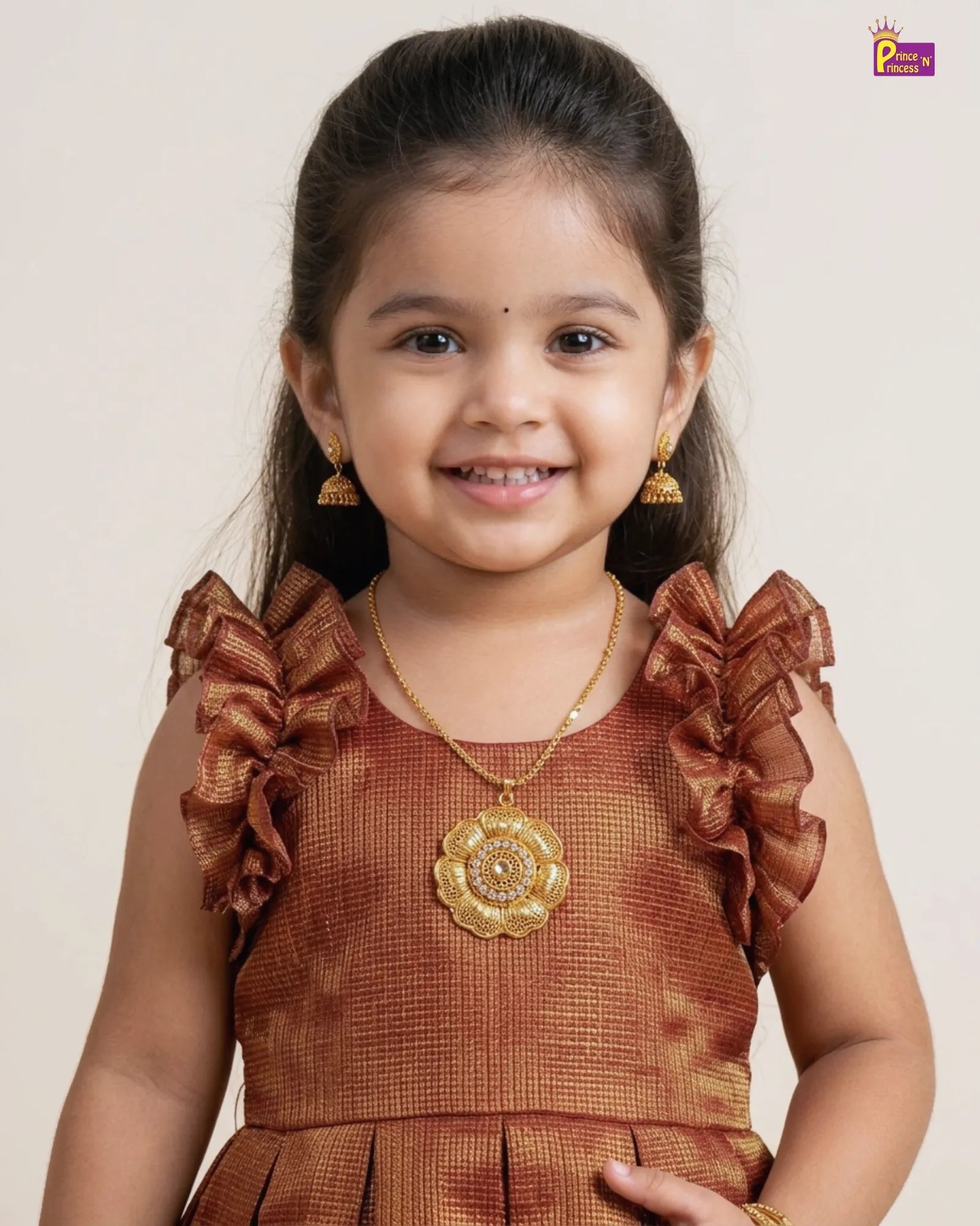 Young girl wearing a brown dress with ruffled sleeves and gold jewelry against a plain background