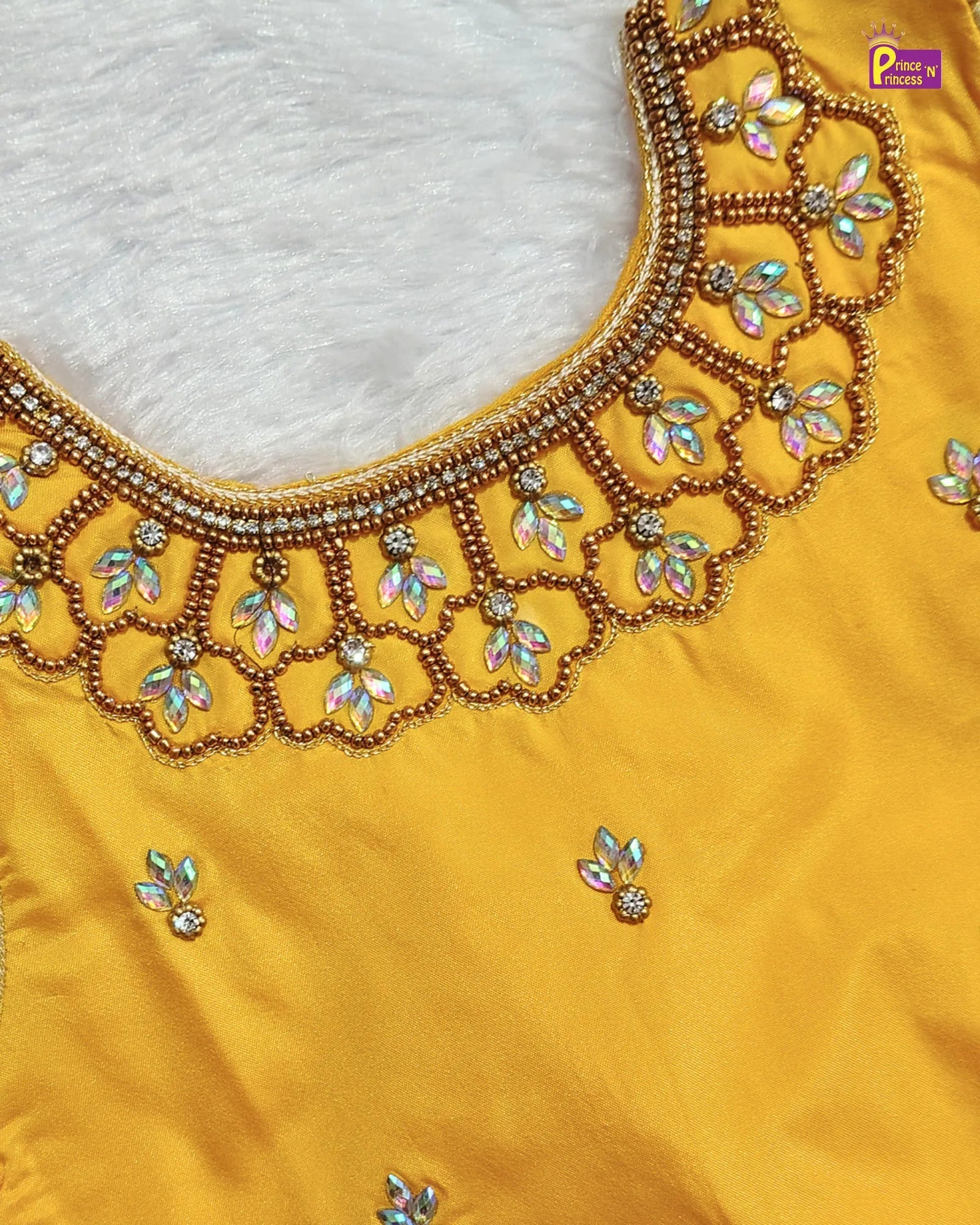 A close-up of a mustard yellow fabric garment featuring an ornate scalloped neckline embellished with gold beadwork, iridescent rhinestones, and small matching embellishments on the body.