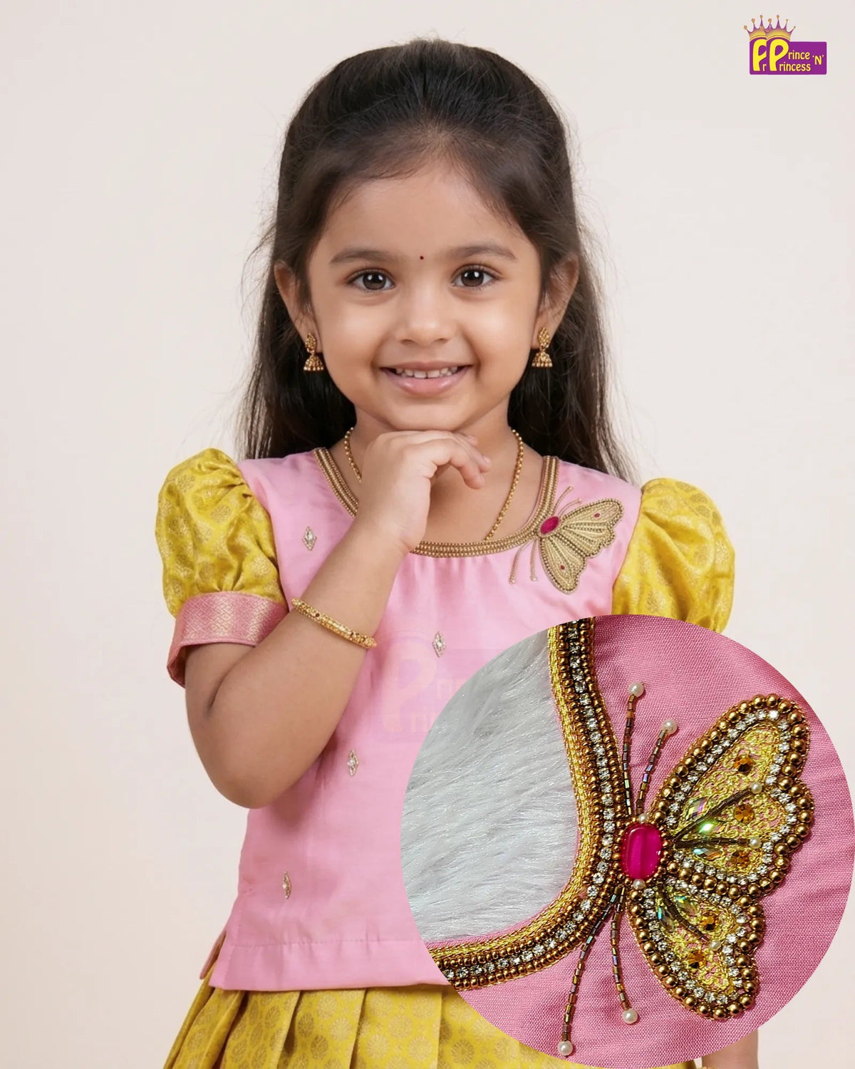 A young girl wearing a pink and yellow traditional outfit with a butterfly embellishment, shown against a plain light background. A circular inset highlights the detailed butterfly embroidery on the pink fabric.