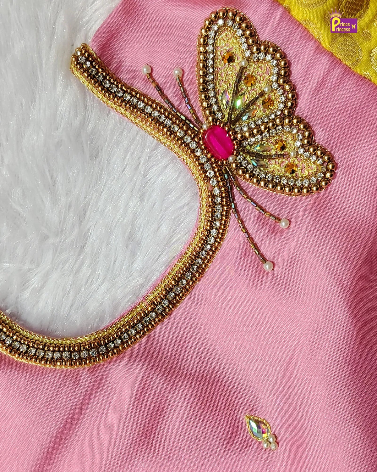 A close-up of a pink fabric garment featuring an ornate gold beaded butterfly embellishment with a pink center stone and rhinestone trim, alongside a small matching embroidered motif near the bottom.